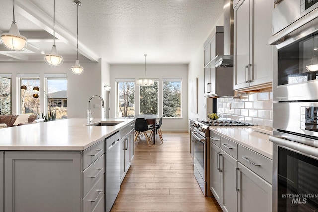 kitchen featuring sink, gray cabinetry, decorative light fixtures, appliances with stainless steel finishes, and a kitchen island with sink