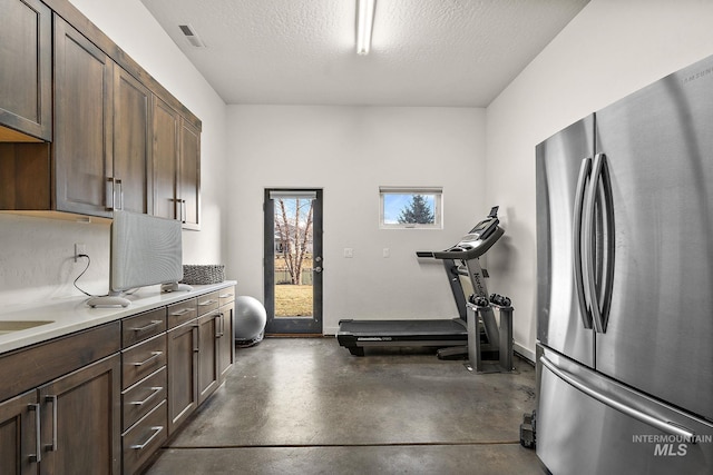 kitchen with stainless steel refrigerator, dark brown cabinets, and concrete floors