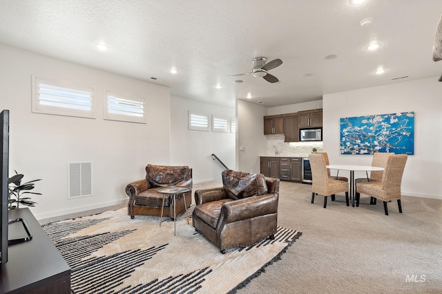 living room with light carpet, ceiling fan, wine cooler, and a textured ceiling