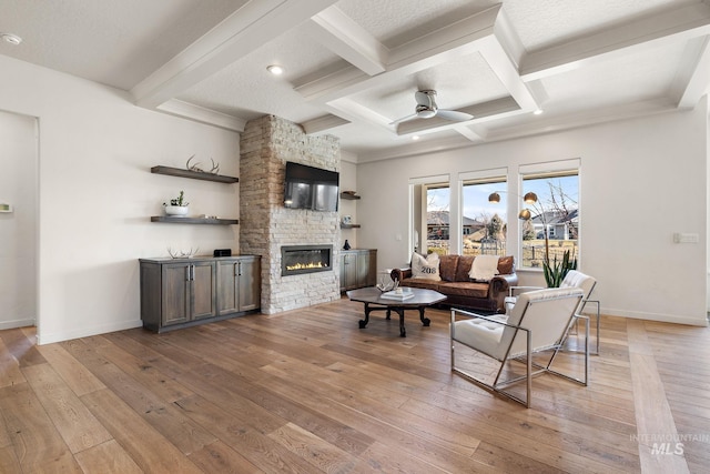 living room with ceiling fan, coffered ceiling, a fireplace, beamed ceiling, and light wood-type flooring