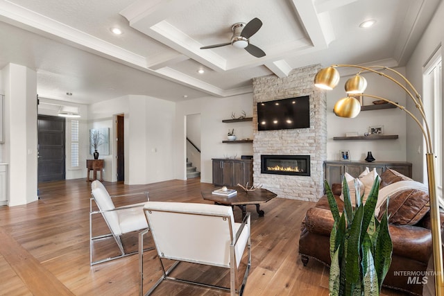 living room featuring ceiling fan, coffered ceiling, wood-type flooring, a stone fireplace, and beamed ceiling