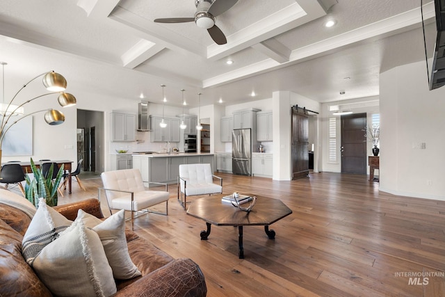 living room featuring coffered ceiling, wood-type flooring, a barn door, and beam ceiling