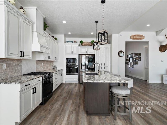 kitchen with white cabinetry, an island with sink, light stone counters, and black appliances