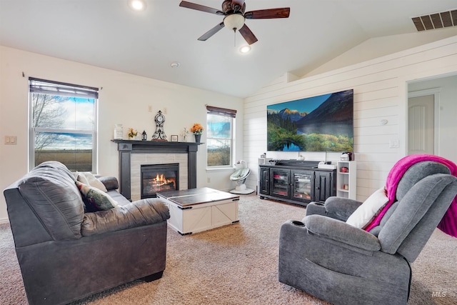 carpeted living room featuring a tiled fireplace, ceiling fan, wood walls, and vaulted ceiling