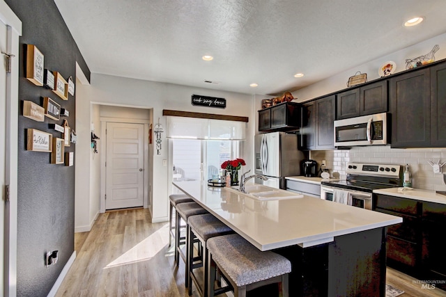 172 S Echo Canyon Ave, Meridian, ID 83642 - kitchen featuring light wood finished floors, an island with sink, stainless steel appliances, a sink, and decorative backsplash