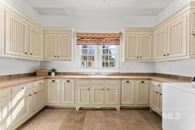 kitchen featuring washer / clothes dryer, sink, and cream cabinetry