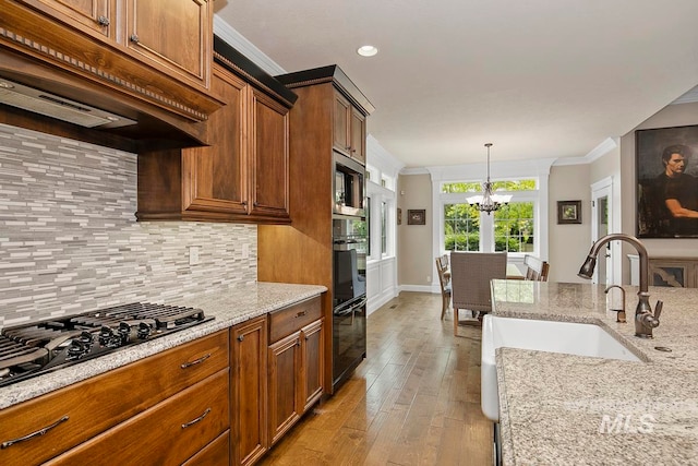 kitchen featuring hanging light fixtures, crown molding, light hardwood / wood-style flooring, black appliances, and premium range hood