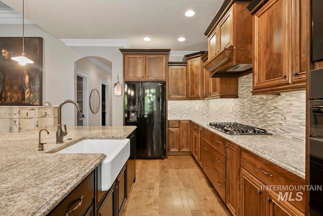 kitchen with light stone counters, light wood-type flooring, decorative light fixtures, and black fridge with ice dispenser