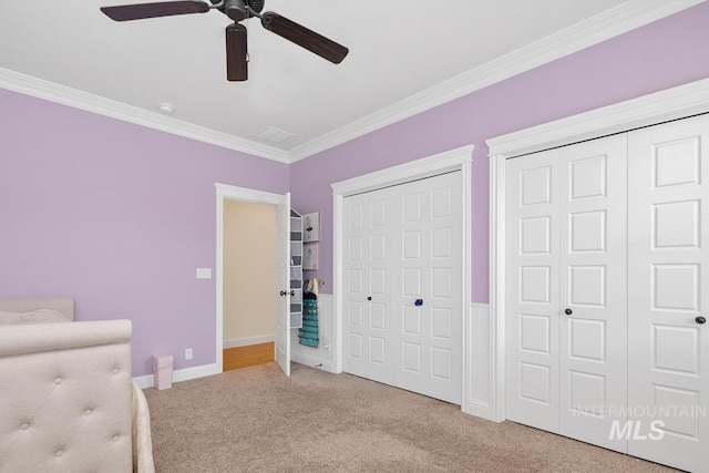 unfurnished bedroom with ornamental molding, multiple closets, ceiling fan, and carpet