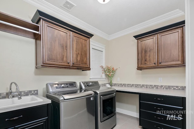 laundry room featuring cabinets, light tile patterned floors, washing machine and clothes dryer, crown molding, and sink