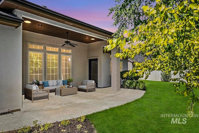 patio terrace at dusk featuring an outdoor living space, ceiling fan, and a yard