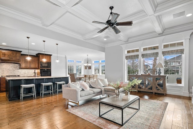 living room with ceiling fan with notable chandelier, coffered ceiling, hardwood / wood-style flooring, and beamed ceiling