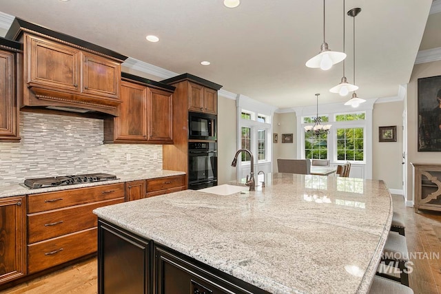 kitchen featuring a breakfast bar area, black appliances, an island with sink, light stone counters, and light wood-type flooring