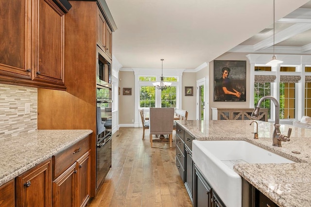 kitchen with light stone countertops, decorative light fixtures, light hardwood / wood-style floors, stainless steel appliances, and sink