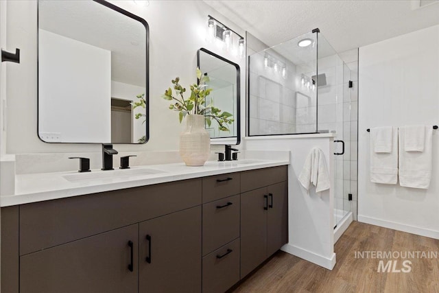 bathroom with vanity, wood-type flooring, a shower with shower door, and a textured ceiling