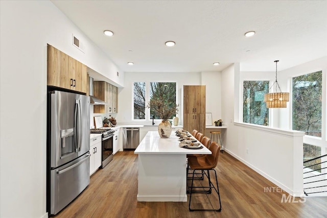 kitchen with a breakfast bar area, appliances with stainless steel finishes, white cabinetry, a kitchen island, and decorative light fixtures