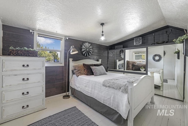 bedroom featuring a textured ceiling, wooden walls, and lofted ceiling