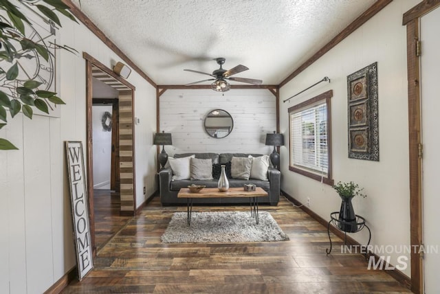 interior space with dark wood-style flooring, ornamental molding, a textured ceiling, wood walls, and ceiling fan