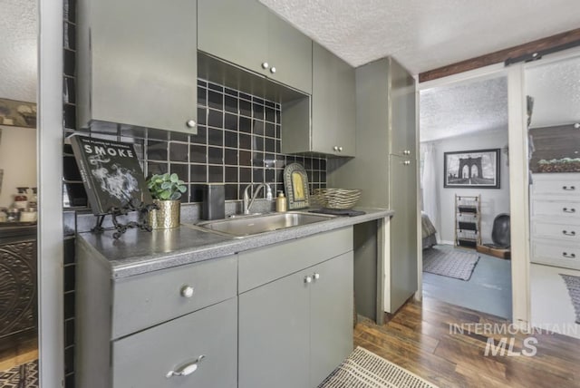 kitchen featuring a textured ceiling, dark wood-style flooring, a sink, decorative backsplash, and gray cabinetry
