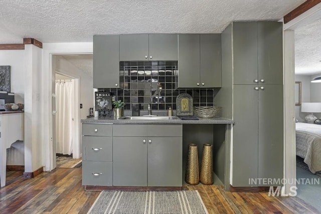 bar featuring dark wood-type flooring, a textured ceiling, a sink, and backsplash
