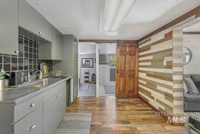 kitchen with a barn door, a sink, gray cabinetry, wood finished floors, and wood walls