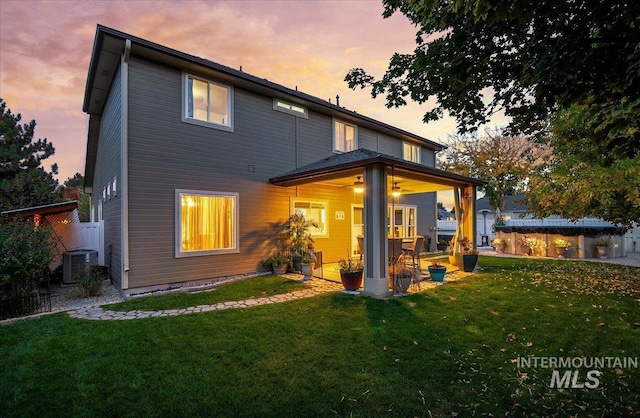 back house at dusk featuring central air condition unit and a yard