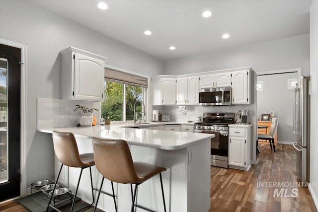 kitchen featuring dark hardwood / wood-style flooring, kitchen peninsula, stainless steel appliances, white cabinets, and a breakfast bar area