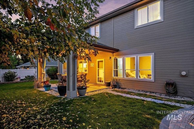 back house at dusk with a patio area and a lawn