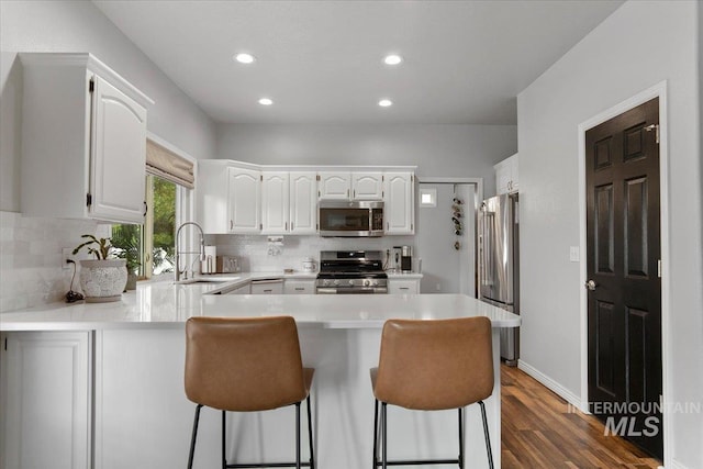 kitchen featuring dark hardwood / wood-style floors, kitchen peninsula, sink, white cabinets, and appliances with stainless steel finishes