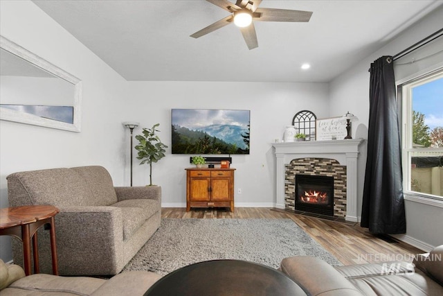 living room with ceiling fan, a stone fireplace, and light wood-type flooring