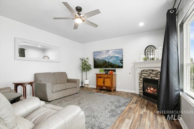 living room with a stone fireplace, ceiling fan, wood-type flooring, and a wealth of natural light