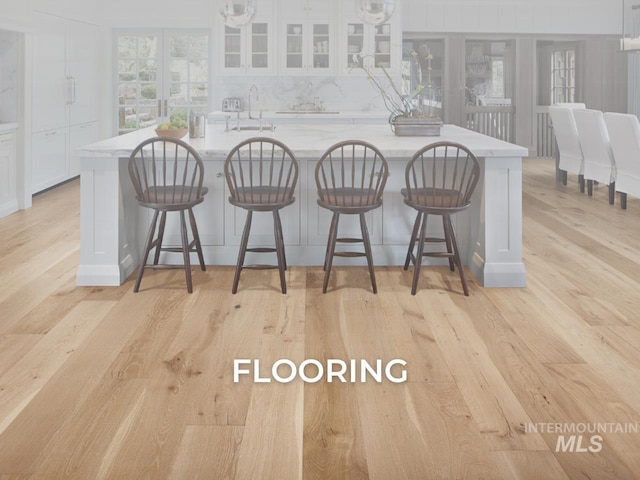 kitchen featuring a sink, light wood-style floors, a large island, white cabinets, and glass insert cabinets