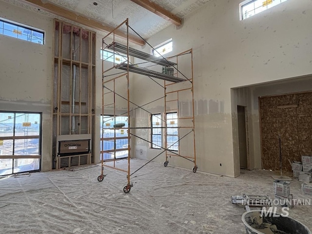 unfurnished living room with a wealth of natural light, a high ceiling, and beam ceiling