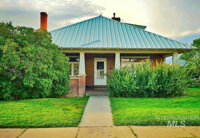 view of front of property featuring a front lawn, a porch, metal roof, brick siding, and a chimney