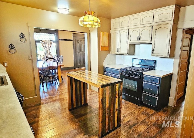 kitchen with black gas stove, dark wood finished floors, hanging light fixtures, white cabinets, and wood counters