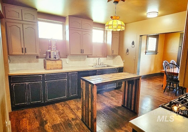 kitchen featuring baseboards, dark wood-style flooring, a sink, hanging light fixtures, and backsplash