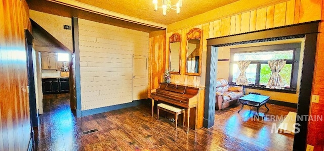 hallway featuring visible vents, wooden walls, an inviting chandelier, and wood finished floors