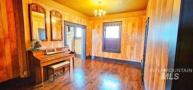 sitting room with wooden walls, a notable chandelier, baseboards, and dark wood-style flooring