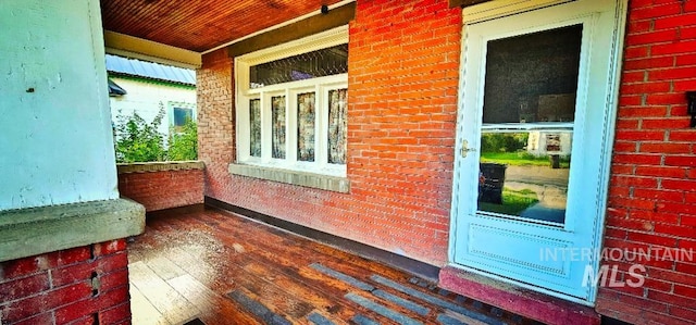 doorway to property with a porch and brick siding