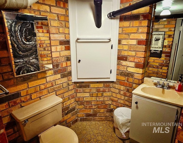 bathroom featuring brick wall, toilet, and vanity