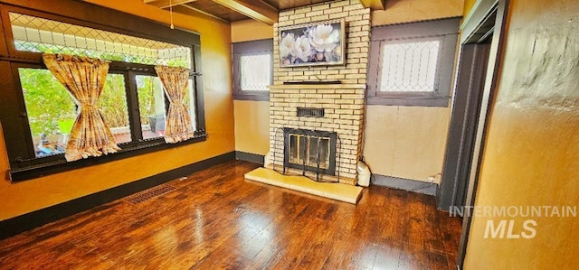 living area with baseboards, wood-type flooring, beamed ceiling, and a fireplace