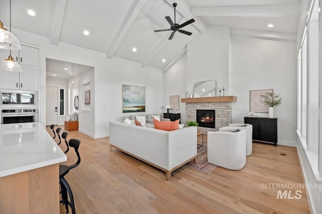 living room featuring beam ceiling, ceiling fan, a fireplace, and light hardwood / wood-style flooring