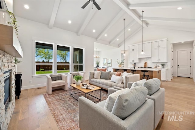 living room with a fireplace, ceiling fan, high vaulted ceiling, beamed ceiling, and light hardwood / wood-style floors