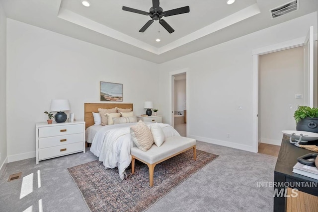 bedroom with ceiling fan, light colored carpet, and a tray ceiling