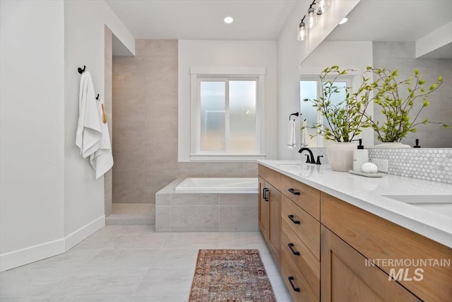 bathroom with tile patterned floors, vanity, and a relaxing tiled tub