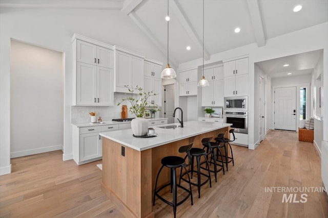 kitchen featuring beam ceiling, white cabinetry, stainless steel appliances, tasteful backsplash, and a center island with sink