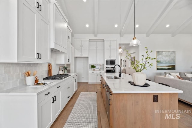 kitchen featuring pendant lighting, white cabinetry, a large island with sink, and beam ceiling