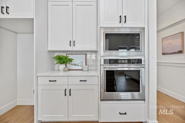 kitchen with stainless steel oven, white cabinetry, built in microwave, and light hardwood / wood-style flooring