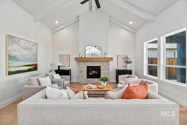 living room featuring beam ceiling, ceiling fan, a stone fireplace, high vaulted ceiling, and light hardwood / wood-style floors