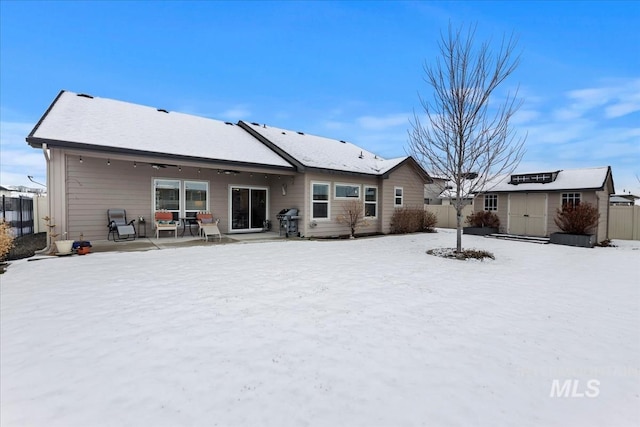 snow covered house with a patio area and a storage unit